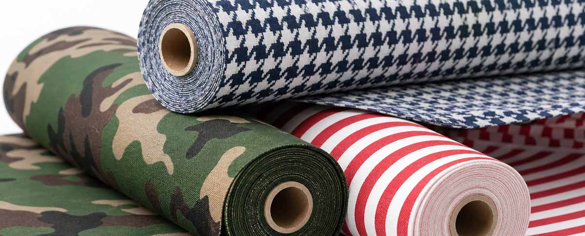 Rolls of printed polyester mini matt fabric showing camo, houndstooth geometric, and stripe patterns for B2B wholesale